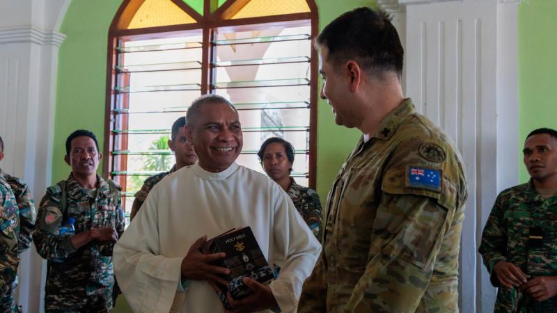 An Australian Army member standing with a Timor-Leste man who is holding a bible.