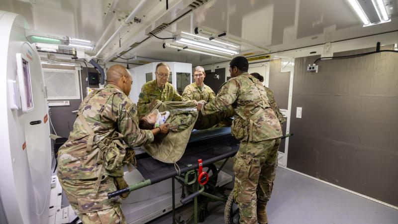 Army officers help load a patient onto a CT machine at field hospital.