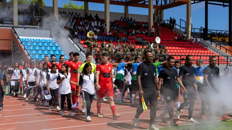 Men in soccer kits walking out onto the field at a stadium, with children in uniform walking next to them.