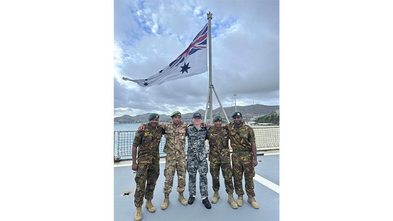 Five men in uniform stand on a ship’s flight deck with their arms around each other’s shoulders.