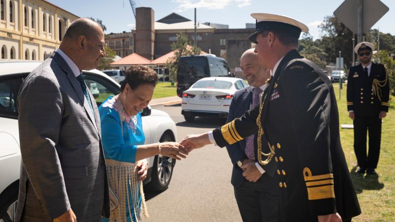 Chief of Navy Vice Admiral Hammond greets Queen Nanasipau’u of Tonga with a handshake. King Tupou VI stands beside her. A man in a suit stands next to the Vice Admiral. A white car is parked behind the Tongan royals in the Garden Island Defence Precinct.