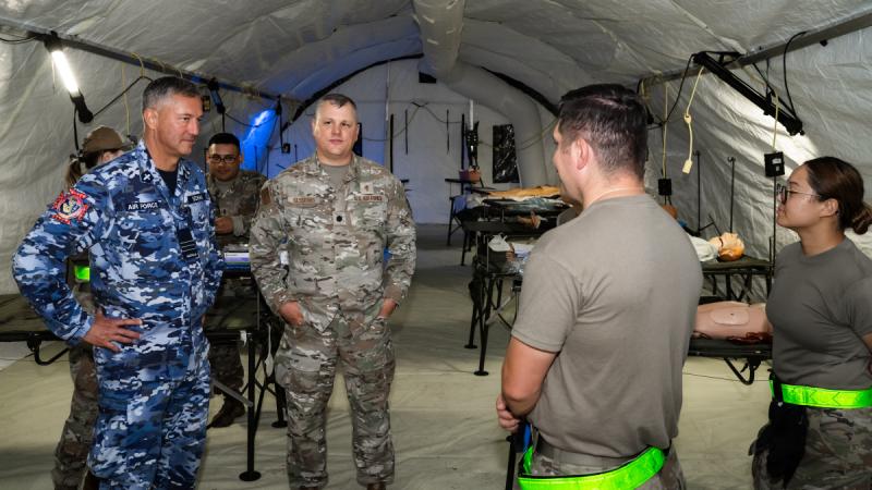 Two chaplains speak US to Air Force personnel in a tented hospital/