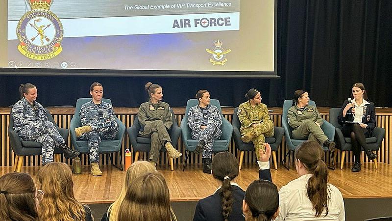 A panel of six women in uniform and a female student sit before an audience.