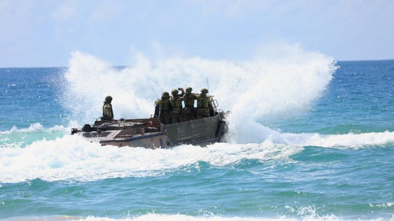 Waves crashing against an amphibious vehicle filled with soldiers as it navigates through the surf.