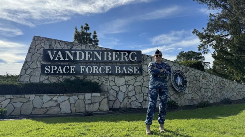 A woman in RAAF uniform stands on the grass in front of the sign for Vandenberg Space Force Base.