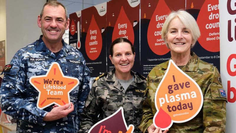 Three people in Air Force, Navy and Army uniforms, respectively, holding signs encouraging people to donate blood.