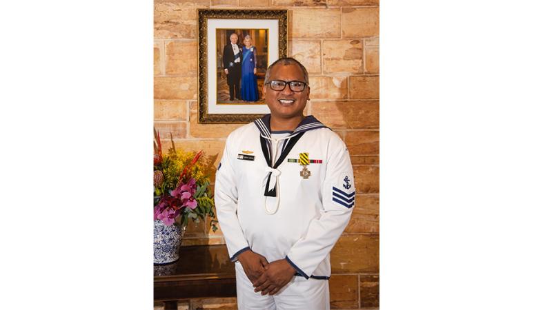 A man in a Navy uniform with a medal displayed prominently on it, smiling for the camera.