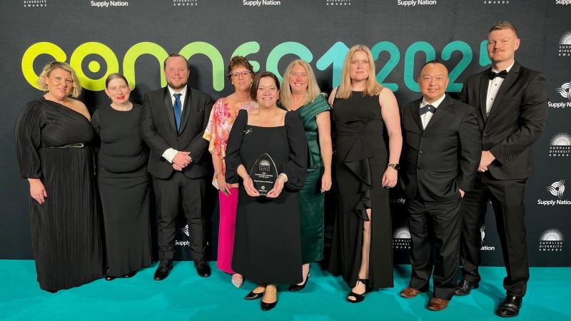 A group of people dressed for a formal event. The woman in the centre is holding an award.