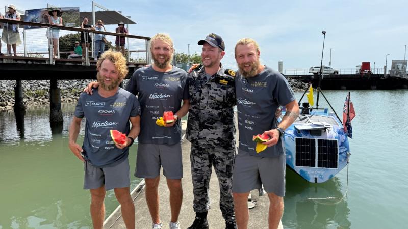 Three rowers line up with a Navy officer on the wharf at Cairns, with an ocean rowing boat moored in the background.