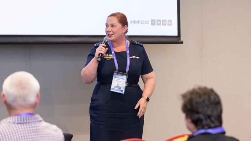 A woman in Air Force uniform addresses a lecture theatre, speaking into a microphone.