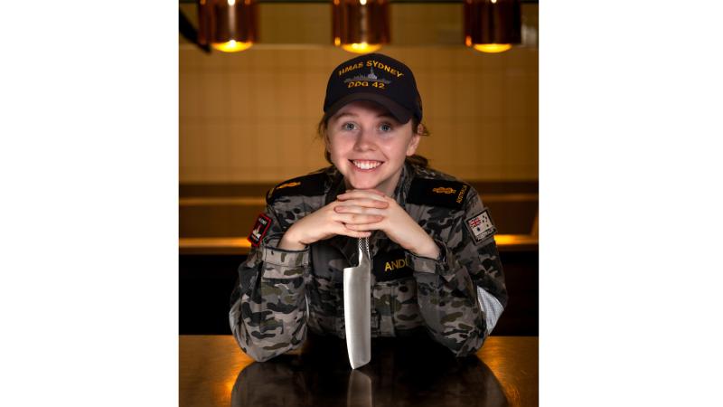 A woman in uniform with a knife in a commercial kitchen.