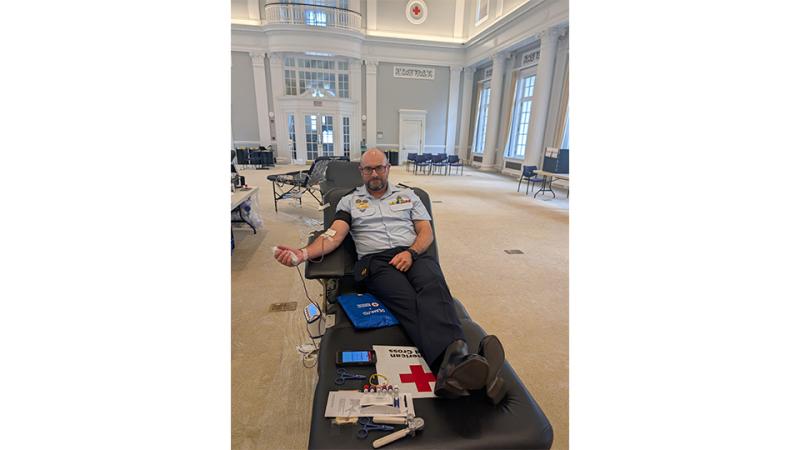 A man lies on a donor bed in a large, sparsely furnished room, as he gives blood.