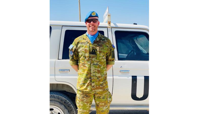 A man in Navy uniform standing in front of a white vehicle.