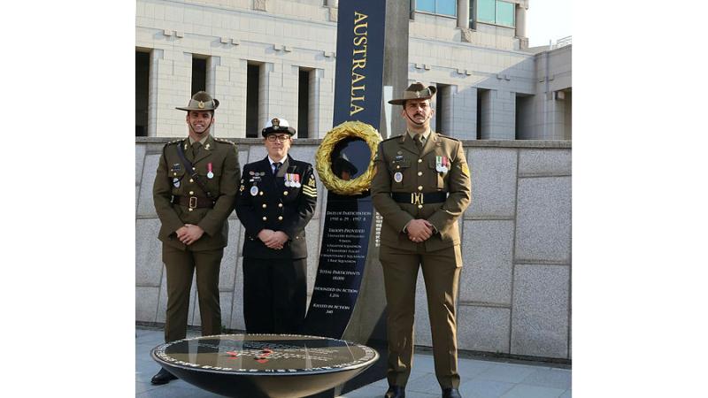 Two Army personnel and one Navy officer stand with a monument at the Australian War Memorial.