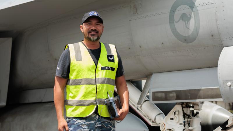 A man in a high-visibility vest stands in front of an aircraft while holding a small electronic device in one hand.