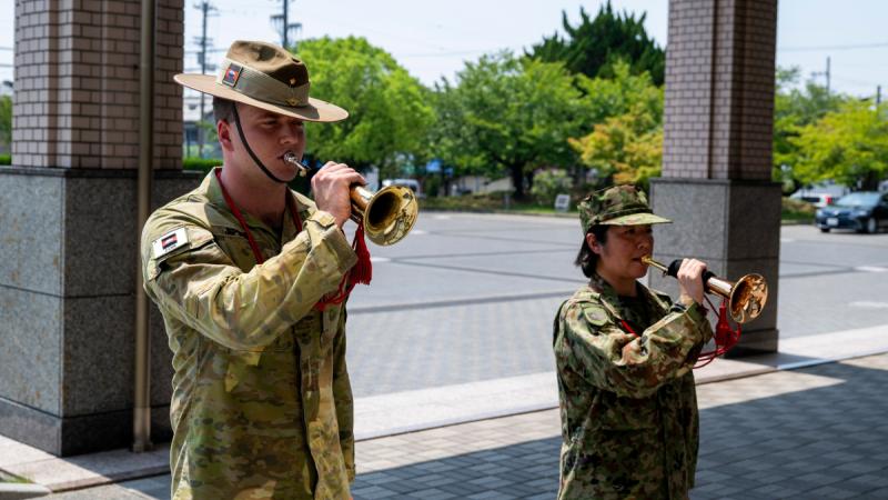 Two people – one man in Australian Army uniform and one woman in Japan Ground Self-Defense Force uniform – playing the bugle.