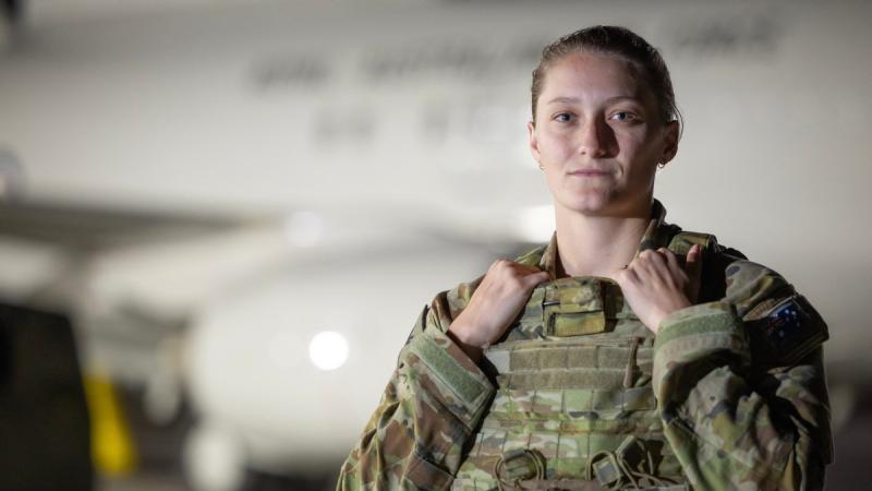 An Air Force security officer in camouflage uniform stands in front of an aircraft .