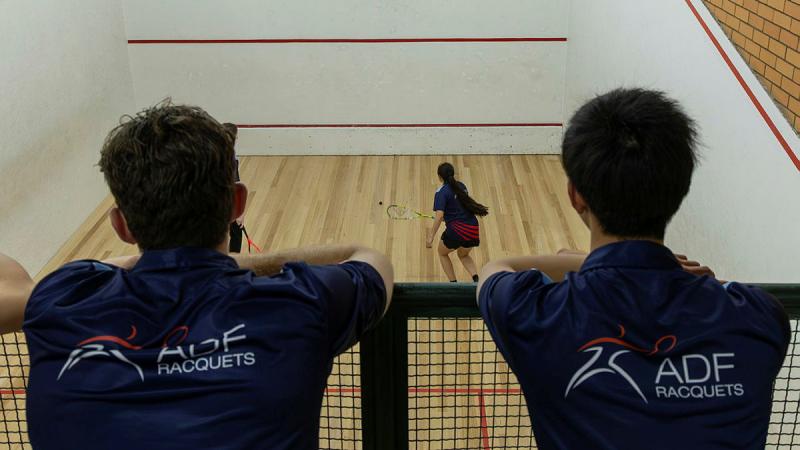 Two ADF members watch another ADF squash player hitting the ball.