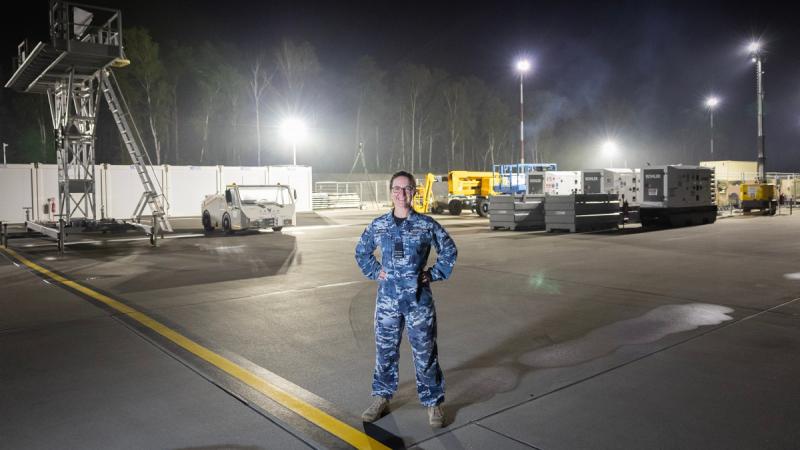 An Air Force officer stands amid an operational airfield in Eastern European, in the dark with floodlights in the background.