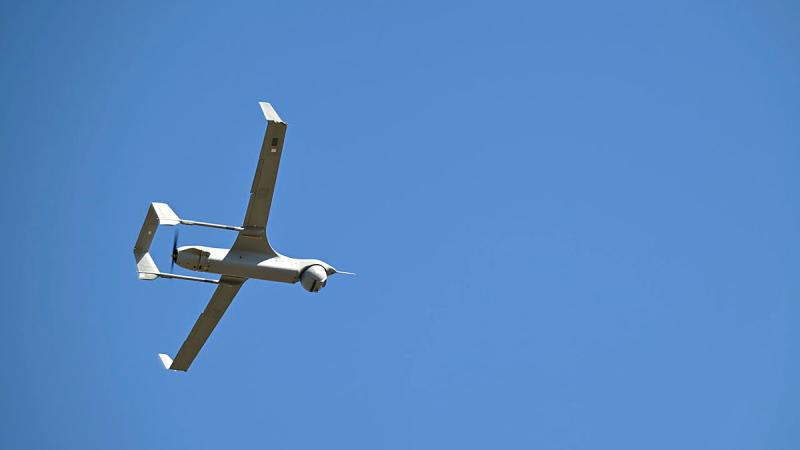 A white uncrewed aircraft flies in a clear blue sky.