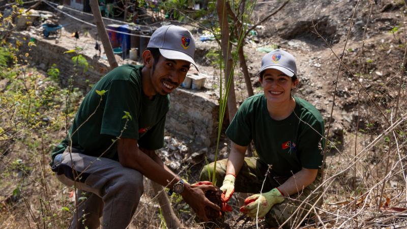 A man and a woman crouch on a hill to plant one vetiver grass plant.