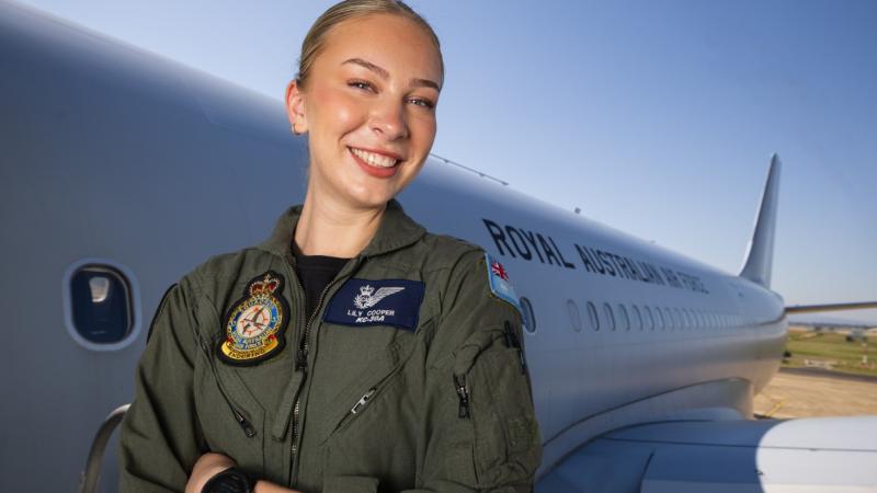 A female crew member in flying suit stands beside an RAAF tanker aircraft.