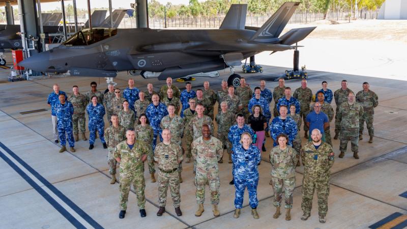 Personnel from the Five Eyes nations stand in five rows in front of an F-35A Lightning II.