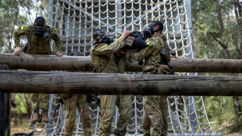 Four people navigate an obstacle course while wearing gas masks.