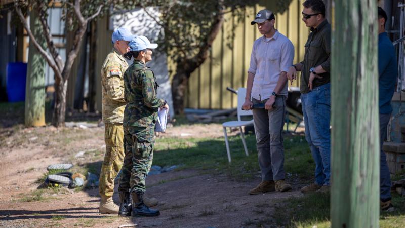 Two people in military uniform wearing light blue caps speak to three men in civilian clothes, one of whom is holding a knife.