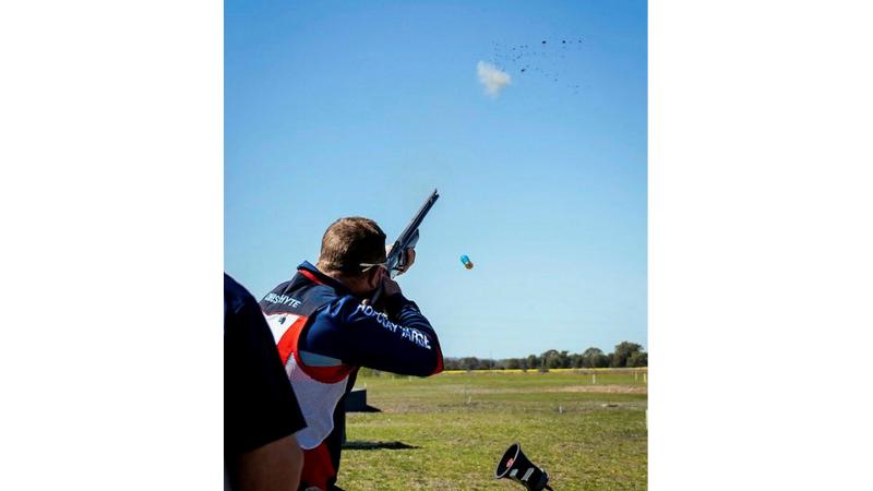 A man points a gun to the sky where an exploded clay target can be seen.