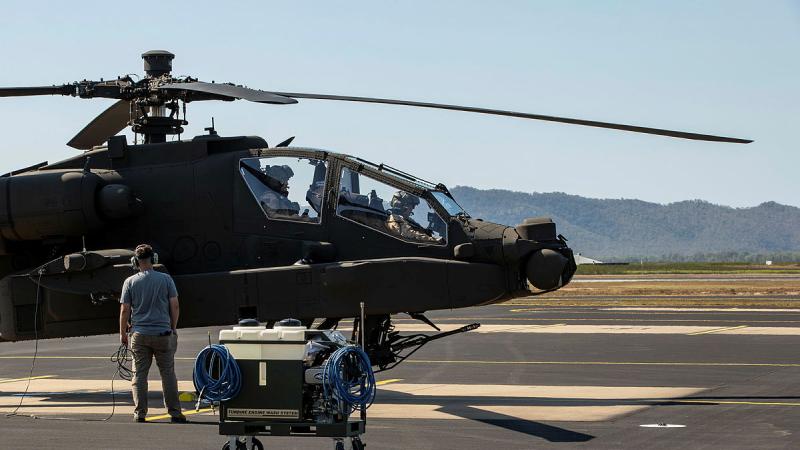 A specialist stands with equipment near a helicopter that is preparing to take off.
