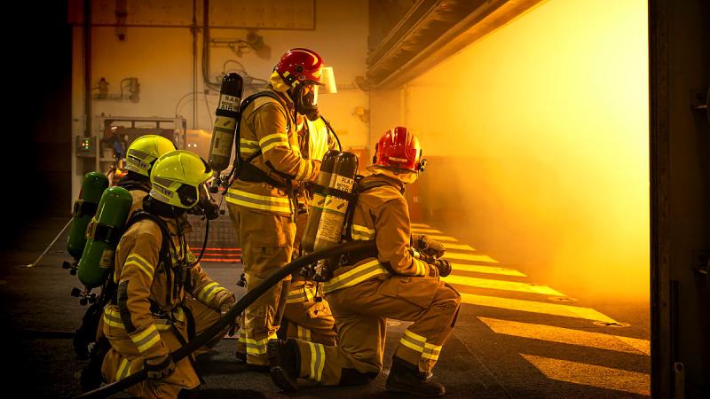 A group of people in firefighting gear face a bright yellow 'fire' light in a firefighting scenario.