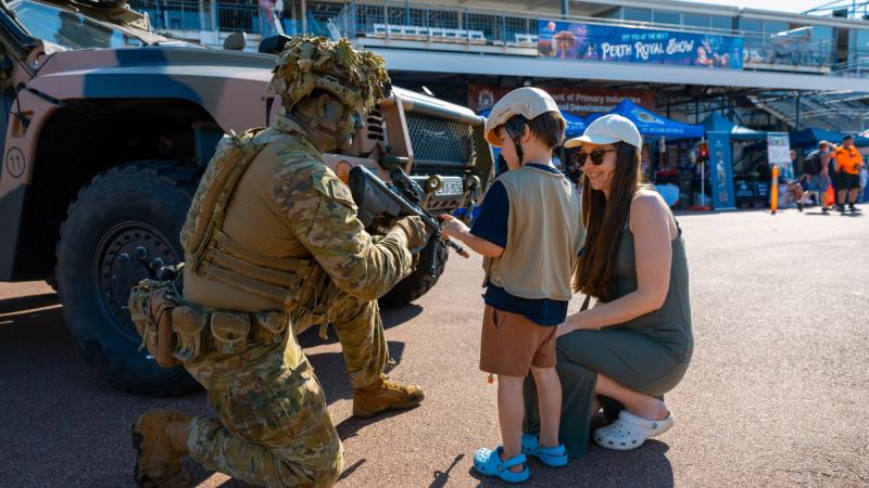 A soldier in combat gear speaks to a mother and child at Perth Royal Show.