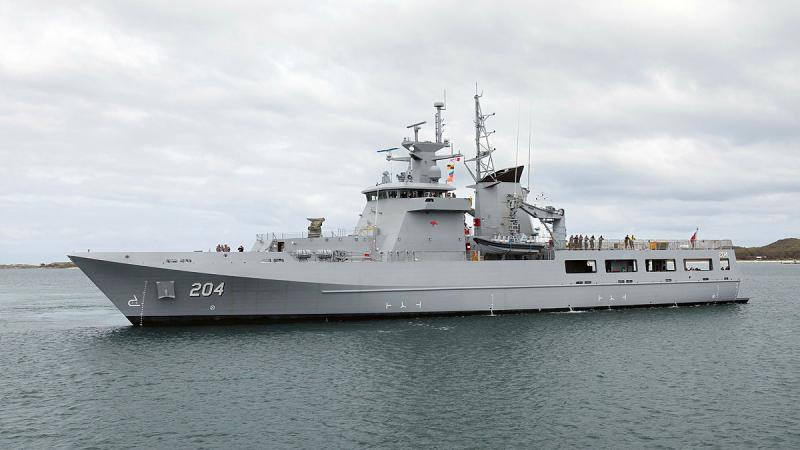 A navy ship sails in blue-grey waters on a cloudy day.