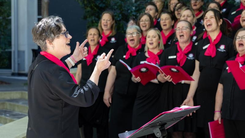 A woman conducts a choir of women.