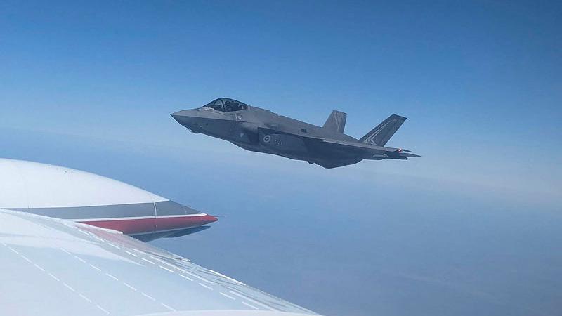 A jet flies through clear skies, viewed from the window of another aircraft.