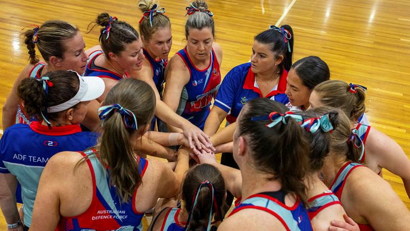 A group of women in netball uniforms for a huddle with their hands on top of one another in the centre of the circle.