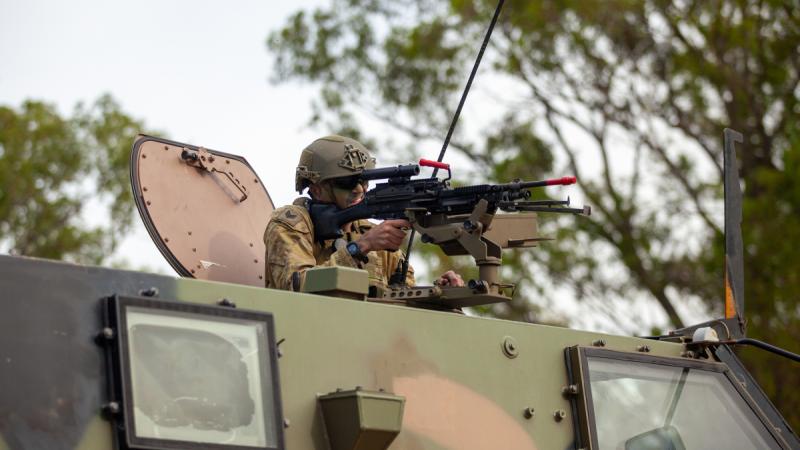 A soldier aims a weapon from the hatch of an armoured vehicle