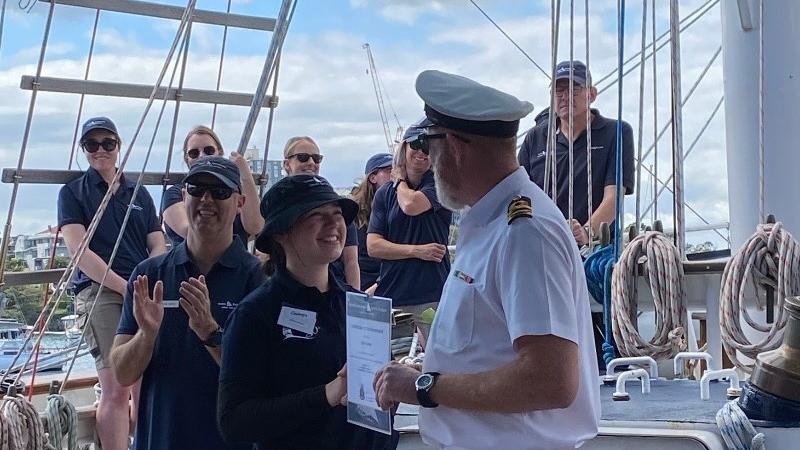 Crew applaud a young woman awarded a certificate on board a sailing ship.
