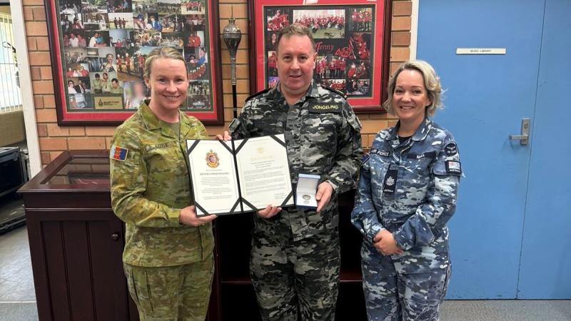 Three Defence personnel in three different service uniforms hold a commendation.