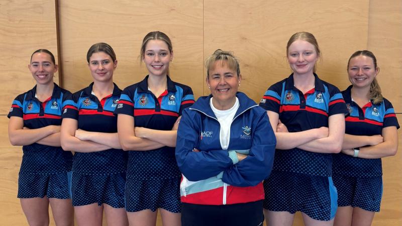 Five netball players and their coach form up in V formation.