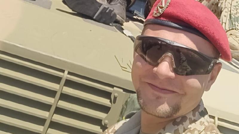 A man in military uniform in front of a vehicle.