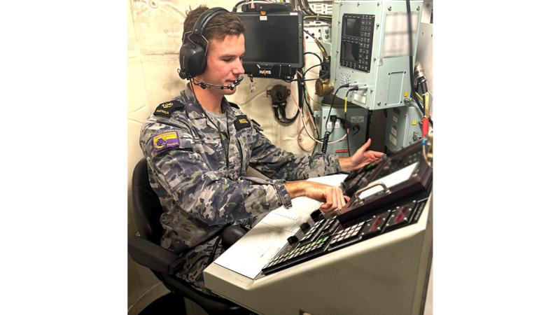 A sailor sitting at a desk with lots of communications controls.
