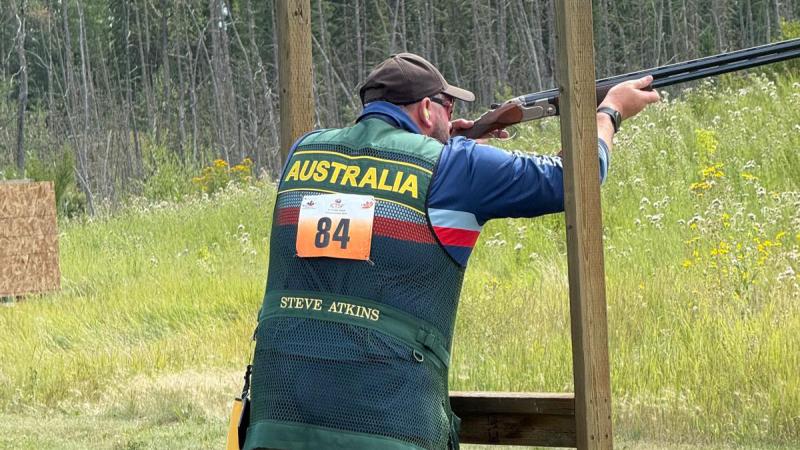 A man stands at a wooden frame and rests his gun to take aim at a clay target.