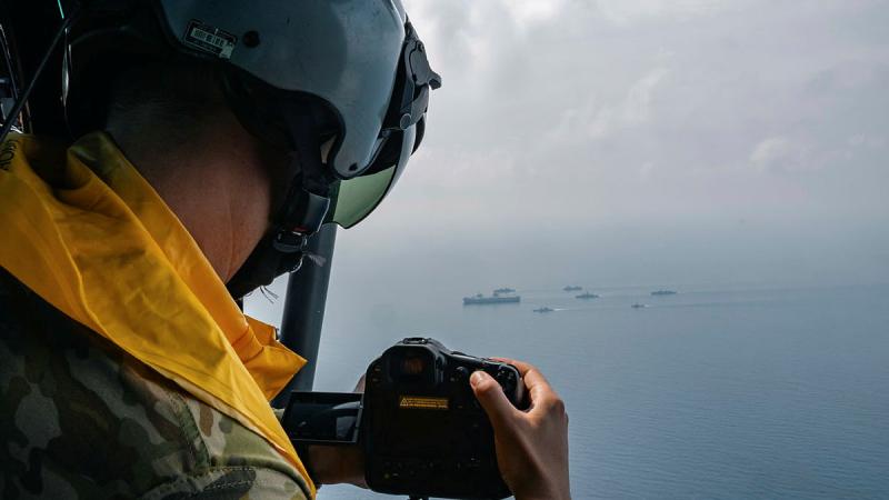 A photographer in a helicopter films navy ships sailing information on open ocean.