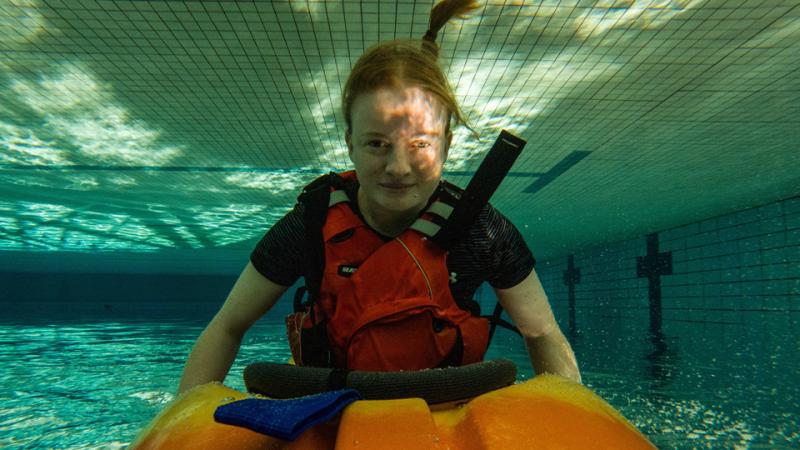 A woman is upside down underwater in a kayak, her ponytail floating above her head.