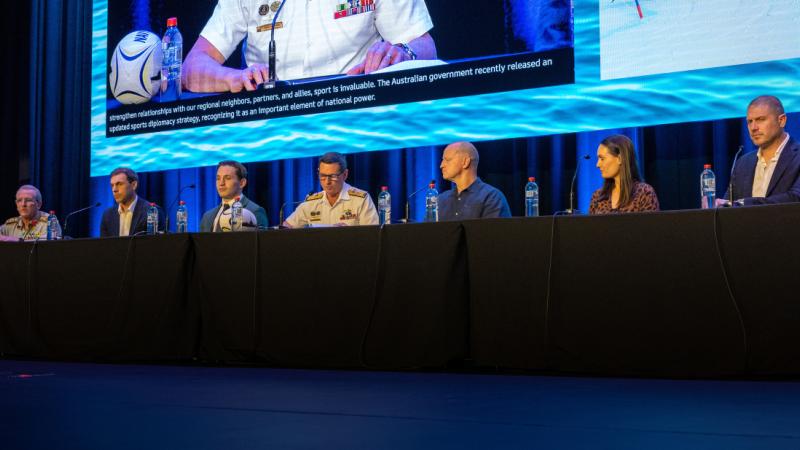 Seven people seated behind a long table on stage, participating in a panel discussion.