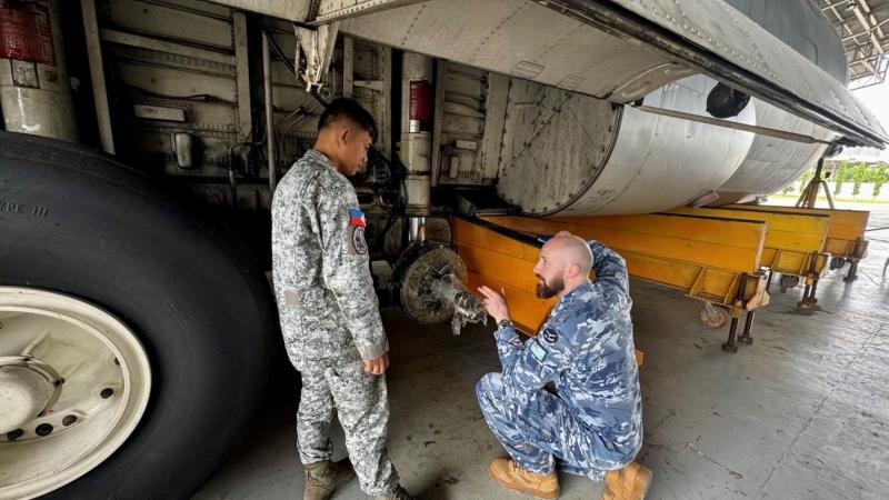 A RAAF aviator points to an axle of a large aircraft while speaking with a Philippine Air Force counterpart.