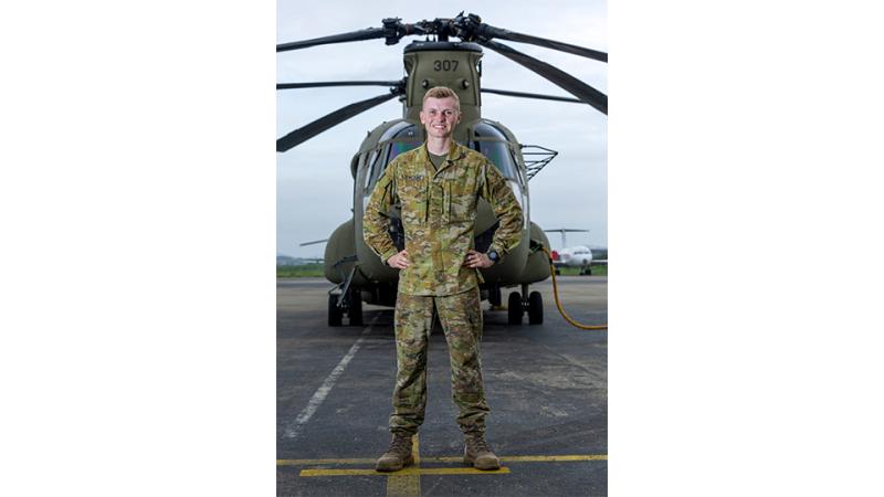 A man in military uniform stands before a helicopter.