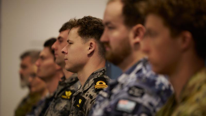 A row of Navy and Air Force personnel sit in a small lecture theatre, listening attentively.